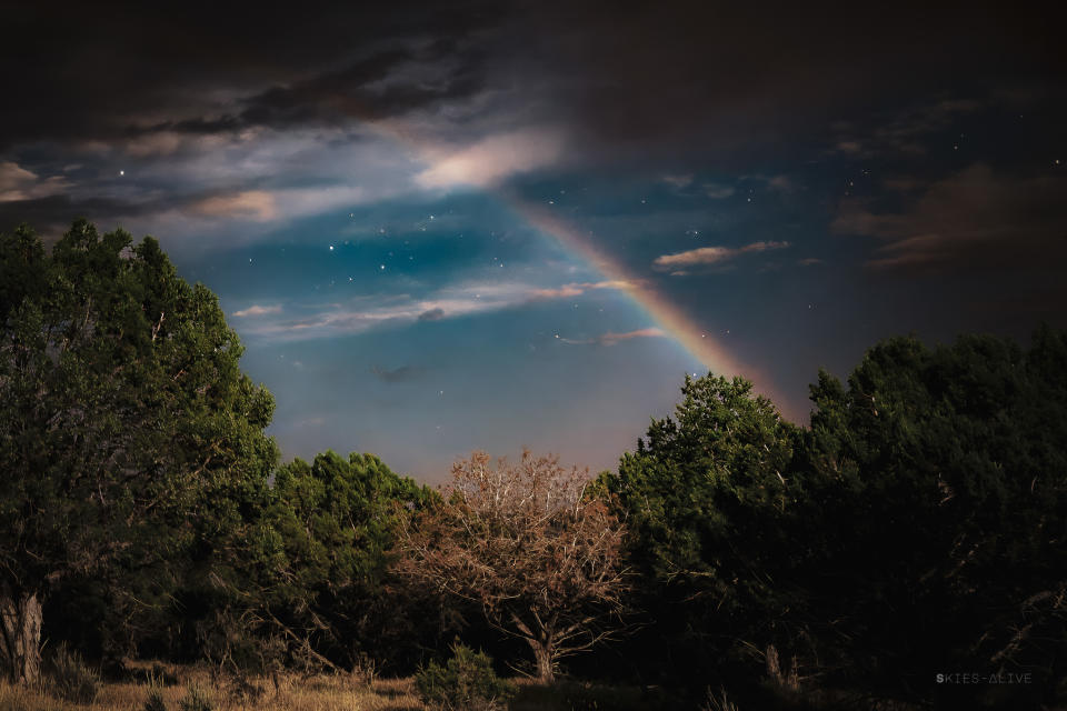 a faint but colorful rainbow emerges and stretches into the night sky with stars behind it.