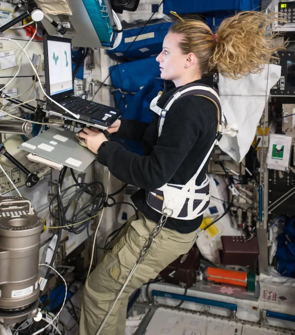 an astronaut looking at a computer screen while floating in a space station module