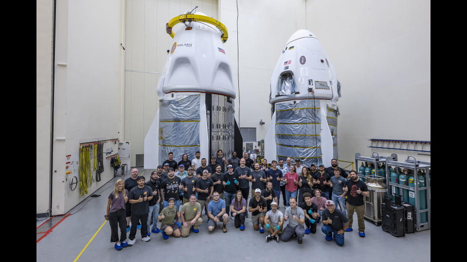 two white space capsules are seen inside a large, white-walled room, with a large crowd of people in front of them