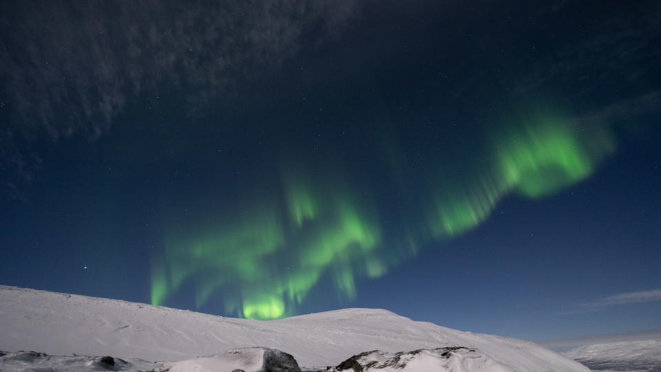 curtains of green light against a clear sky with snow capped mountains below.