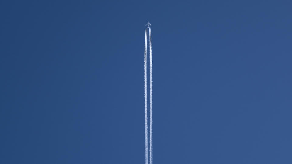  Up the center in a vast blue sky two white lines of smoke trail a small airlpaine near the top of the image. 