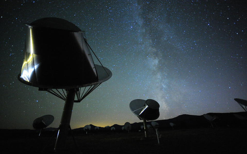  Radio telescopes point up at the dark night sky with mountains in the background. 