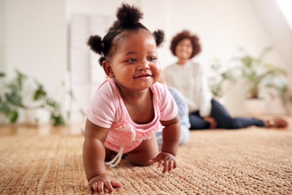 baby crawls toward camera with woman out of focus in background