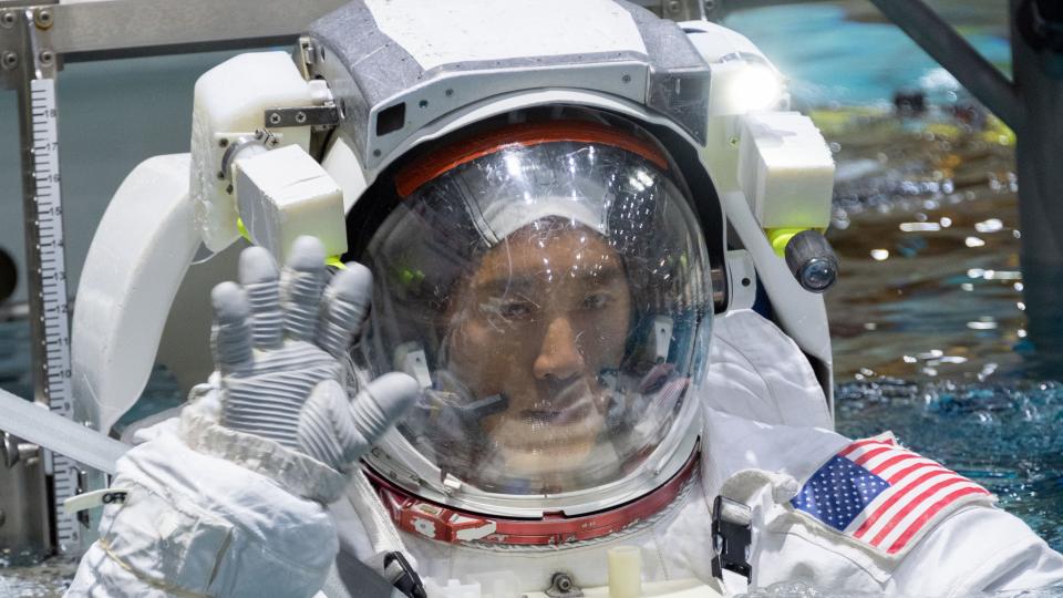  An astronaut in a spacesuit in the harness in the water, waving at the camera . 