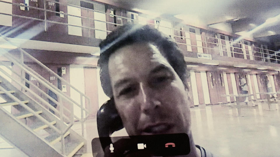 In a grainy image, Scott Peterson holds a phone to his ear in what appears to the interior of a jail.