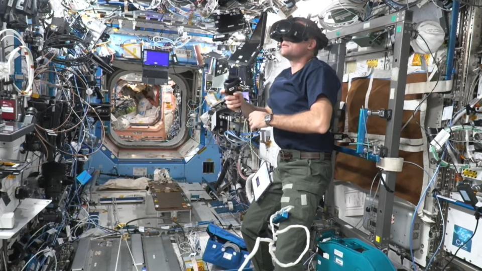  An astronaut wearing a virtual reality headset in a crowded space station module. 