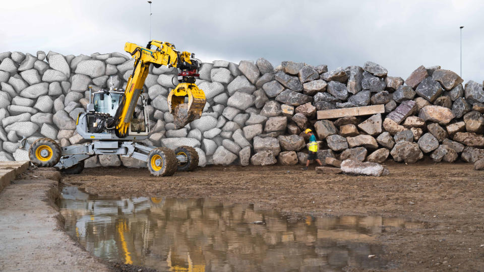  A yellow excavator holds a large boulder, part of its effort to build a rock wall. 