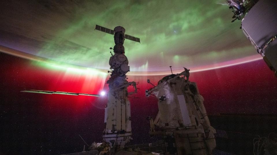 an aurora on earth as seen from the space station. various space modules are in front