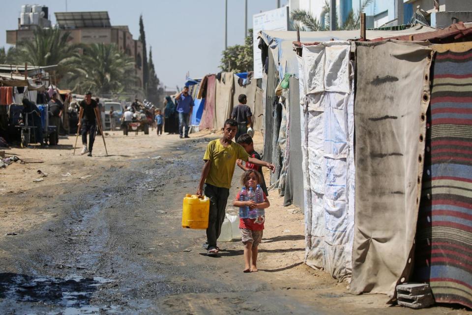 PHOTO: Displaced Palestinian children haul water to their tent in a makeshift camp in the perimeter of the Al-Aqsa Martyrs Hospital in Deir al-Balah in the central Gaza Strip following renewed Israeli evacuation orders for the area on Aug. 26, 2024. (Eyad Baba/AFP via Getty Images)