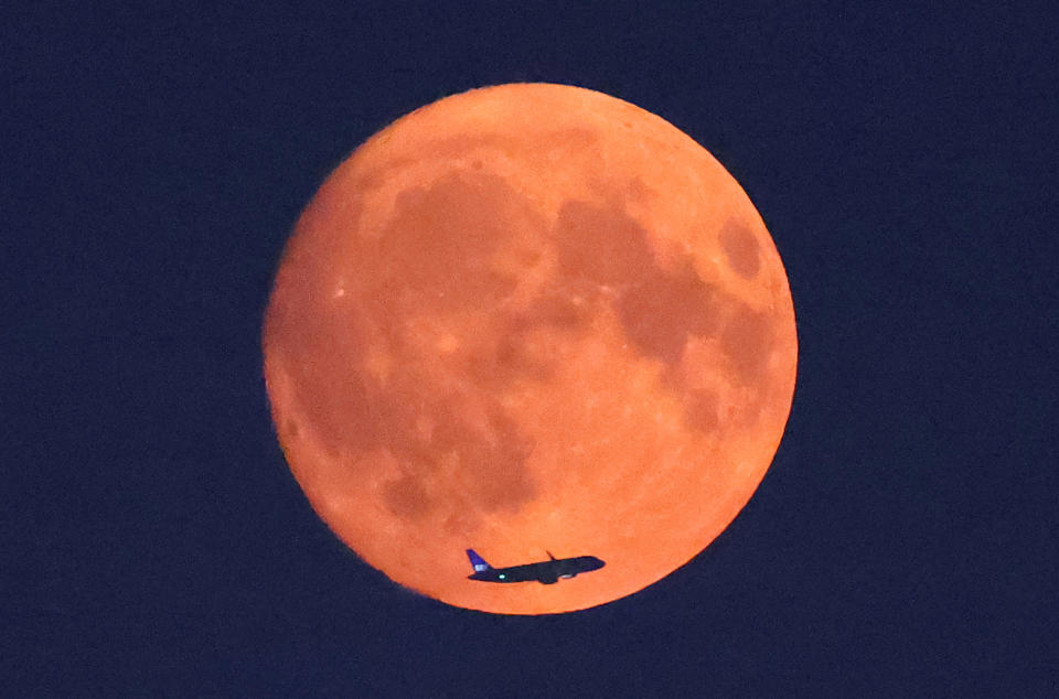 An aircraft passes in front of the moon, with a red glow attributable to smoke particles carried in the upper atmosphere from North American wildfires, a day ahead of the full super moon, as seen from Parliament Hill in London, Britain, Aug. 18, 2024. / Credit: Toby Melville/REUTERS