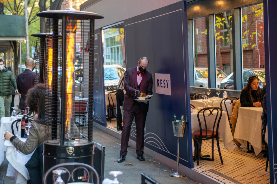 NEW YORK, NEW YORK - NOVEMBER 29: An employee wearing a mask lights a birthday candle outside an American Express and Resy-sponsored outdoor dining area at Carbone on November 29, 2020 in New York City. The pandemic continues to burden restaurants and bars as businesses struggle to thrive with evolving government restrictions and social distancing plans which impact keeping businesses open yet challenge profitability. (Photo by Alexi Rosenfeld/Getty Images)