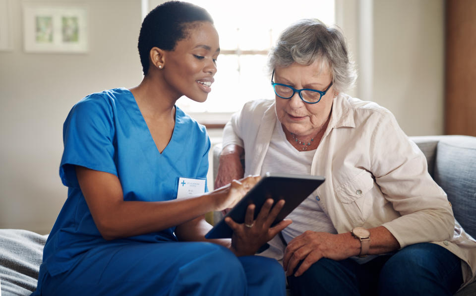 Shot of a senior woman using a digital tablet with a nurse on the sofa at home