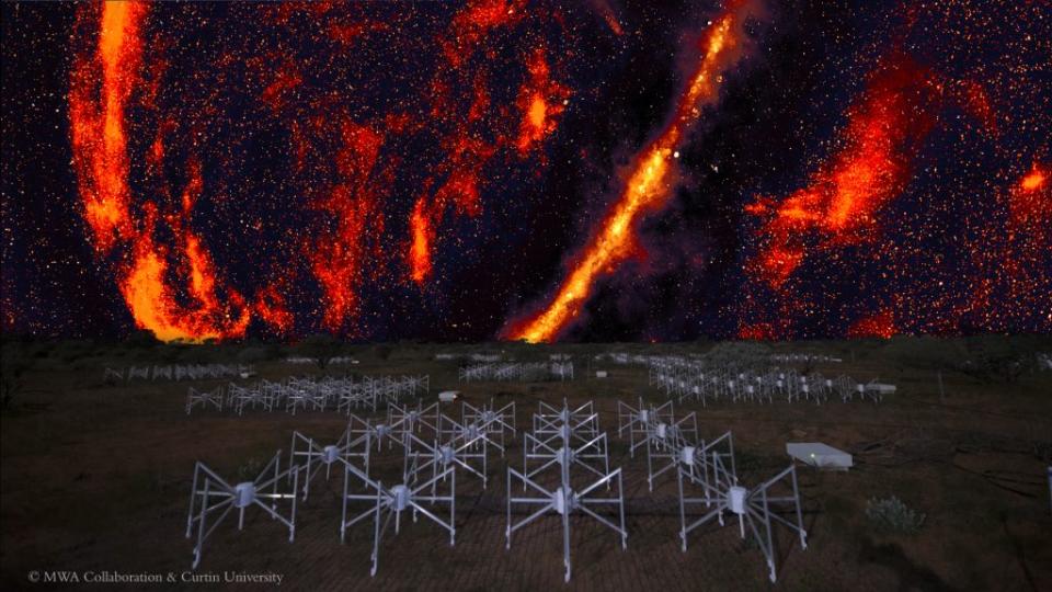  The sky looks dark with red glowing streaks. On the ground, there are a bunch of gray structures that together make up the MWA. 