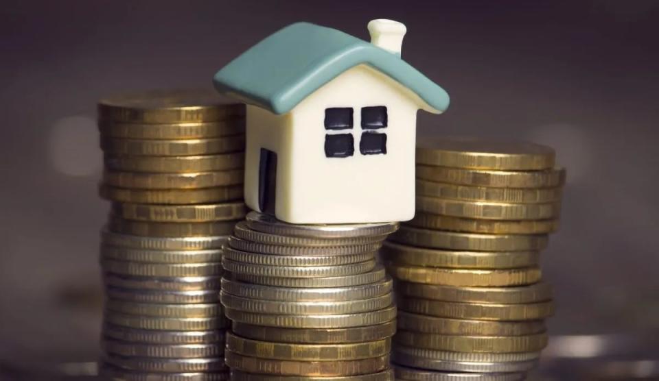 small model house on top of a stack of coins buying power