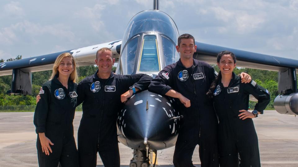  Four people in dark jumpsuits lean on a jet. 