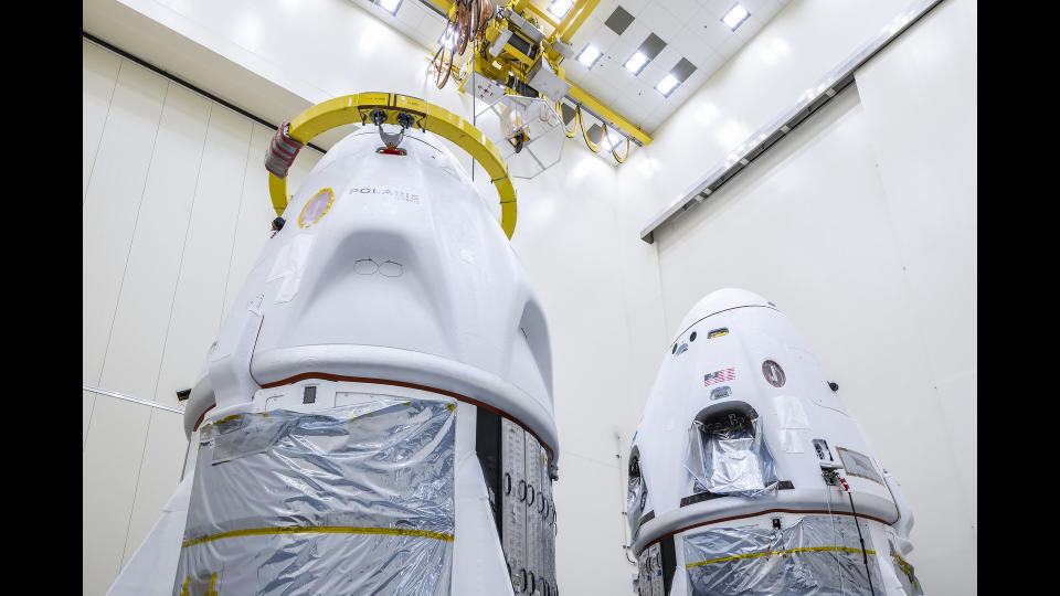  Two white space capsules are seen inside a large, white-walled room. 