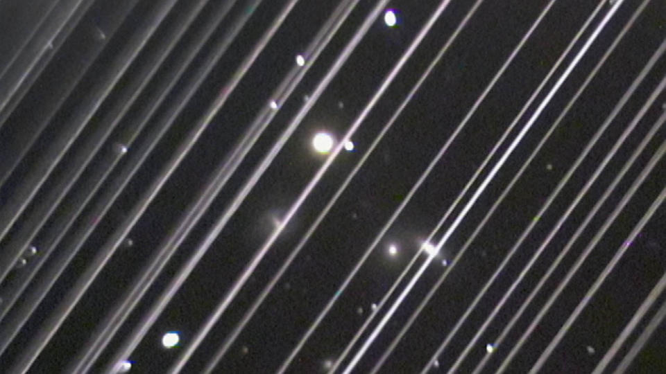  An image of the night sky marked by two dozen diagonal white lines, caused by the movement of satellites. 