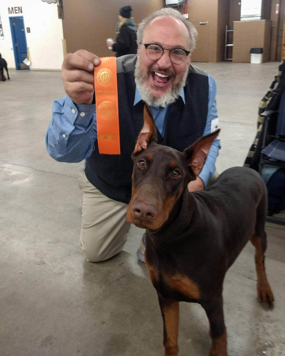 Paul Peavey holds an award while kneeling behind a Doberman (Elite European Dobermans)