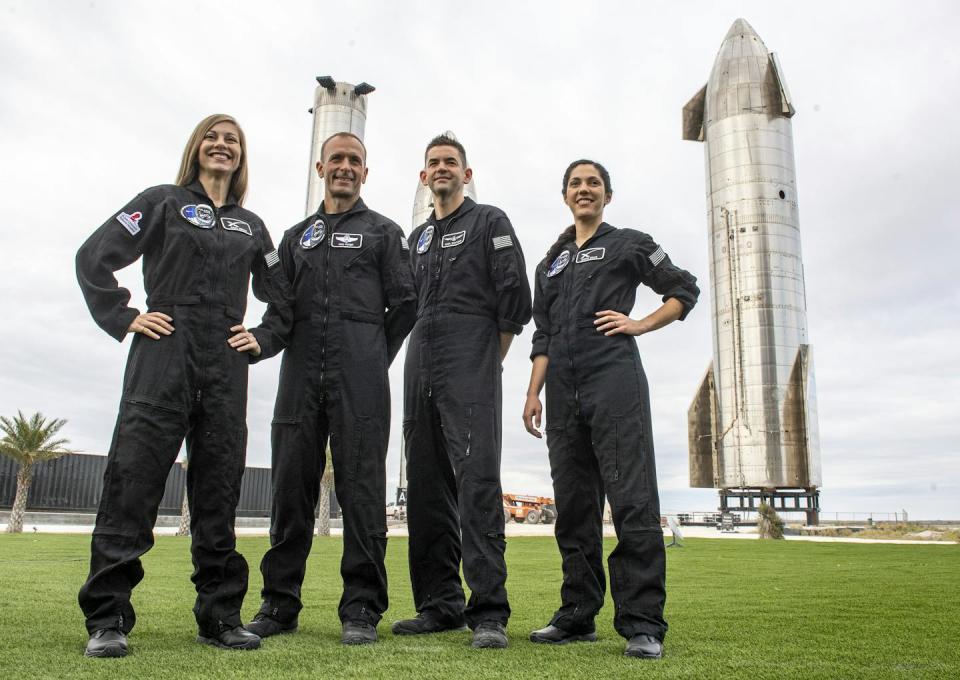 Two men and two women wearing black jumpsuits stand together on a lawn.