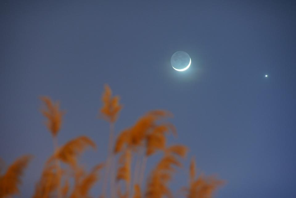 a thin crescent moon in the sky with a bright orb beside it