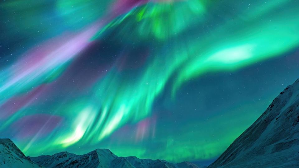  Ribbons and curtains of light in the sky colored green, purple and pink. There are snow-capped mountains below. . 