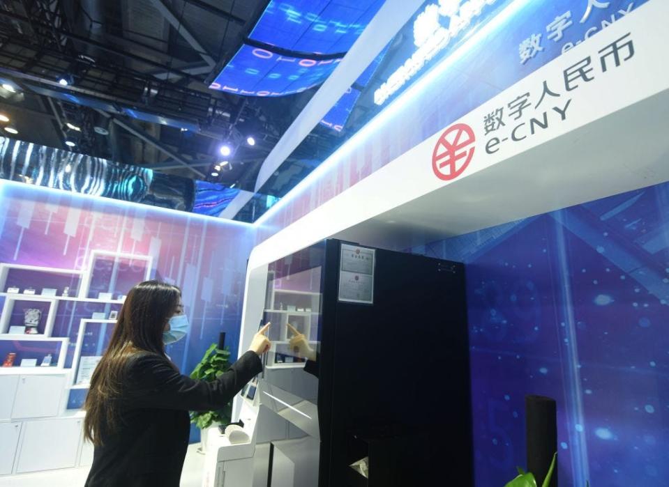 Woman with a face mask using a touch screen at an exhibition booth for the e-renminbi.