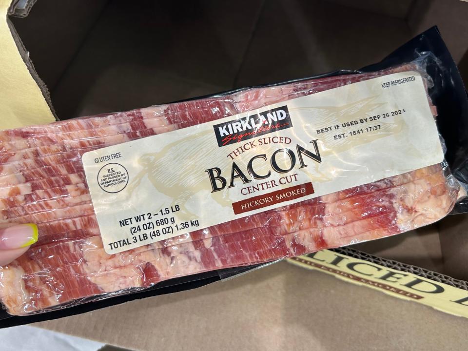 Lara holding a pack of Kirkland Signature thick-cut, Hickory-smoked bacon at Costco.