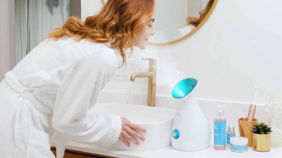 Someone in a robe using the facial steamer in a bathroom