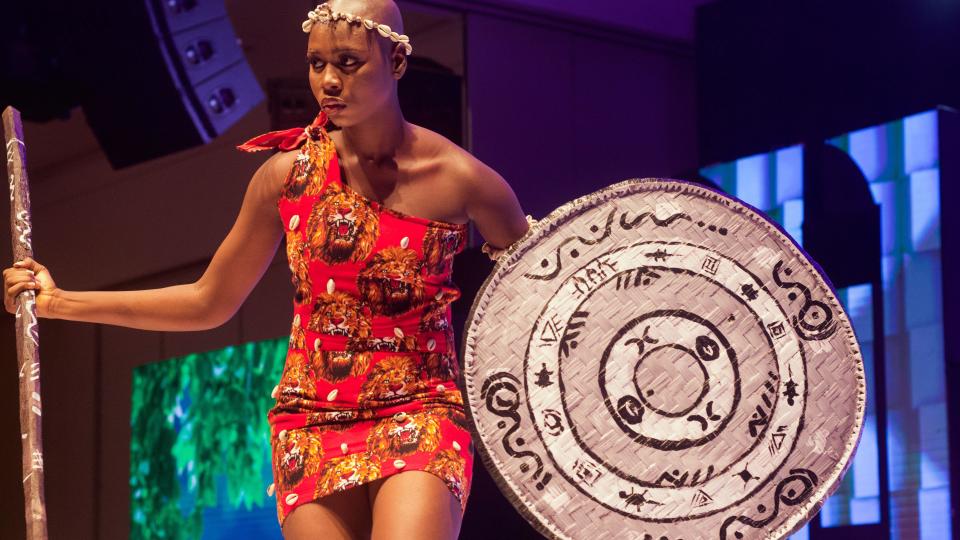 A Miss Universe Nigeria contestant wearing a beaded headband, a red dress with lion print and a silver shield with tribal markings at the pageant in Lagos, Nigeria - Saturday 31 August 2024