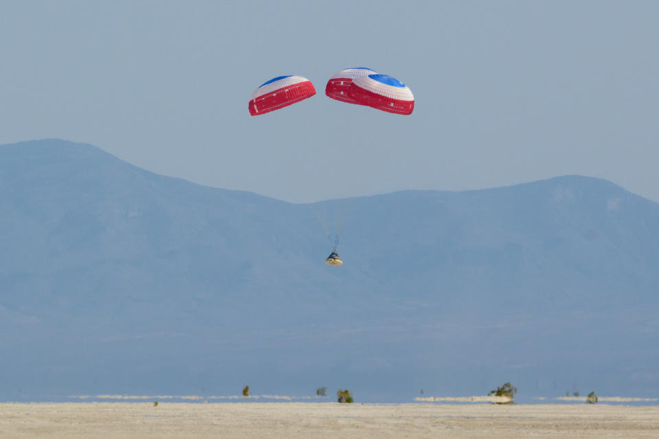 parachutes above a cone-shaped spacecraft, hovering above a desert, with mountains in the background