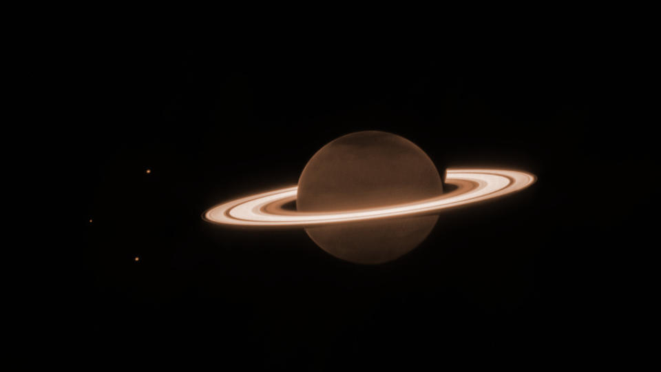 saturn, its rings and three moons stand out against the blackness of space in this james webb space telescope photo