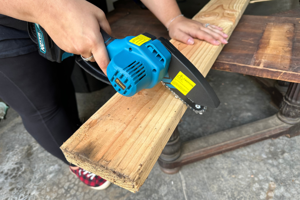 the writer using the mini chainsaw to cut into a wooden plank