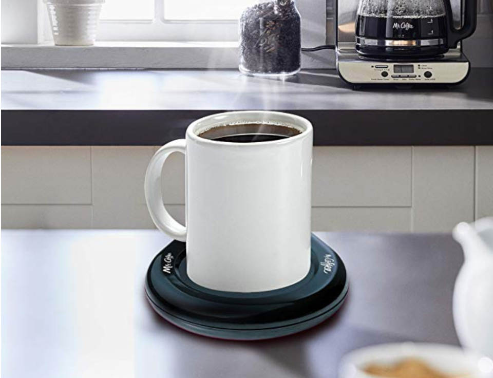 A steaming cup of coffee on a counter, sitting in a Mr. Coffee mug warmer. 