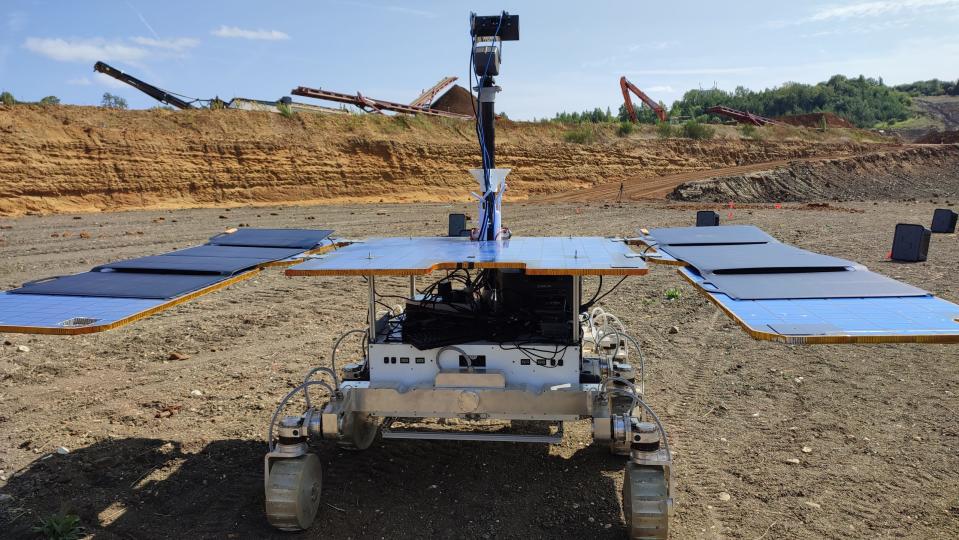 a four-wheeled rover drives in red dirt on a construction site