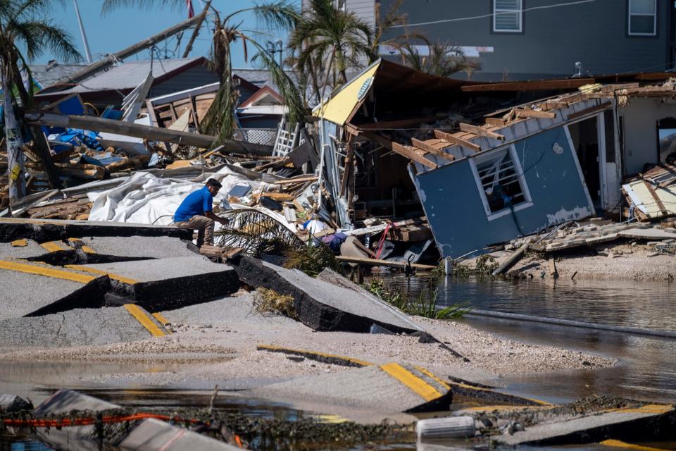 A man sits on a broken section of the Pine Island Road in the aftermath of Hurricane Ian