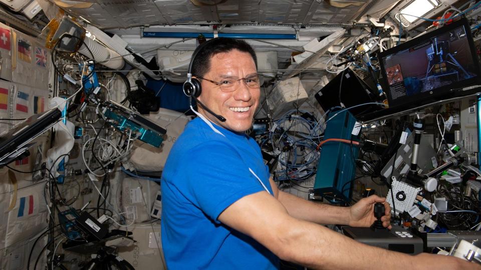 an astronaut floating in spies smiles while handling laboratory equipment