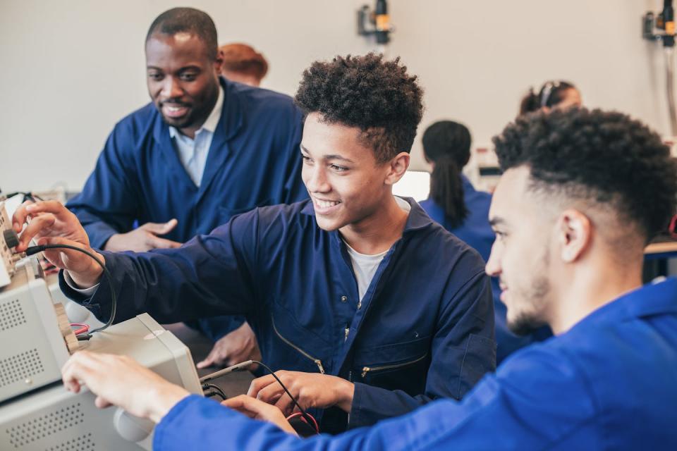 Two engineering students put wires into a computer as an instructor looks on.