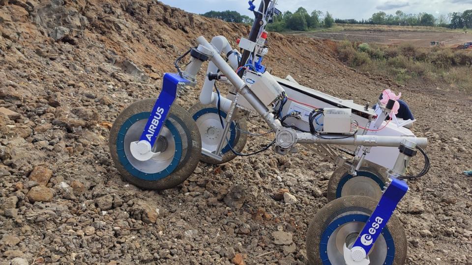  A four-wheeled rover drives in red dirt on a construction site. 