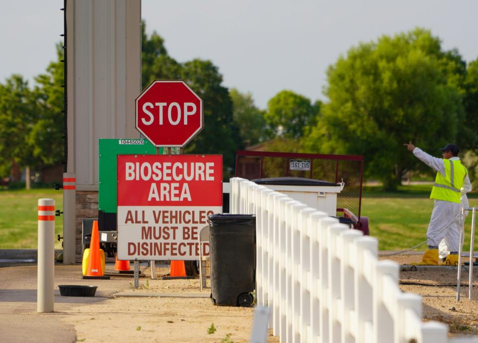 A federal worker with the Animal & Plant Health Inspection Service wearing a protective suit and with boots sealed with tape gestures at a checkpoint to the entrance of a Weld County, Colorado, chicken farm. The "biosecure" sign is part of the farm's normal entry signage but federal officials were monitoring the farm on Tuesday, July 30, 2024.