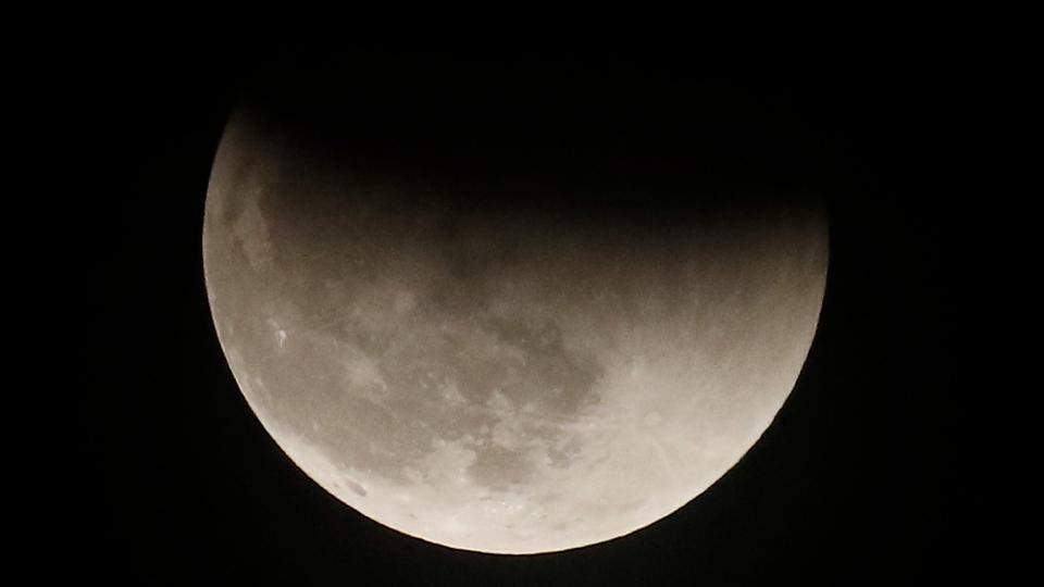  The moon in a dark sky. the top edge of the moon darkened by a shadow. 