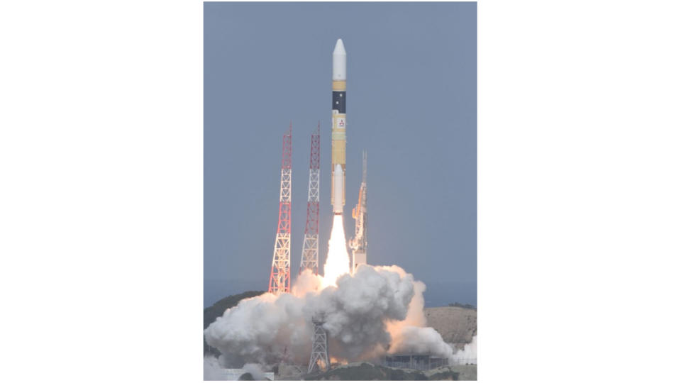  A yellow and white rocket launches into a blue sky. 