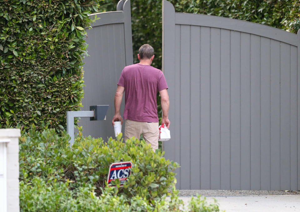 Ben Affleck from behind, holding fast food items while standing at an open gate.