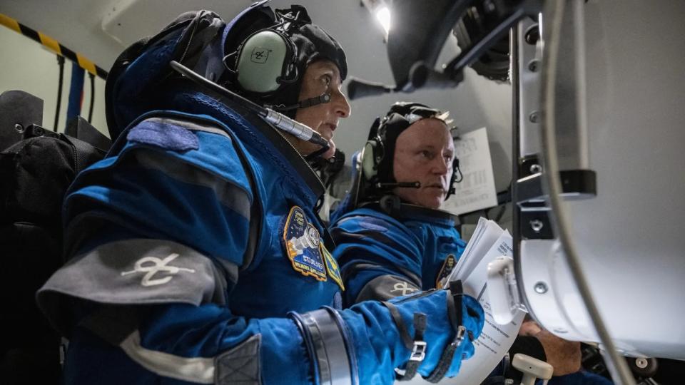  Two astronauts in spacesuits looking at a simulator screen. 