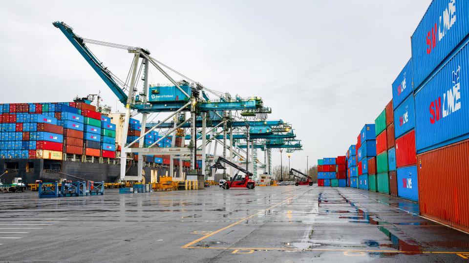 Image shows wet pavement, containers, and container cranes.