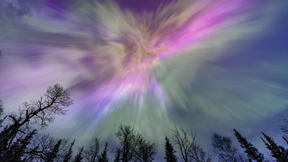  Northern lights appear over a lake in Minnesota in a dark sky overhead shining rainbow of Aurora light with trees below. . 