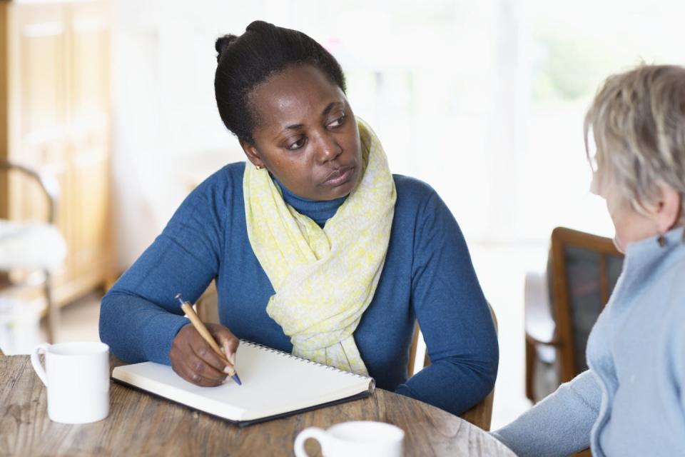 Two women are sitting at a table and one of them is using a pencil to take take notes.