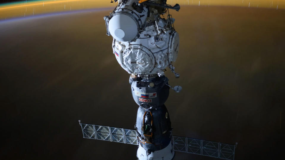  A gray and white spacecraft is seen against the curve of earth at night. 