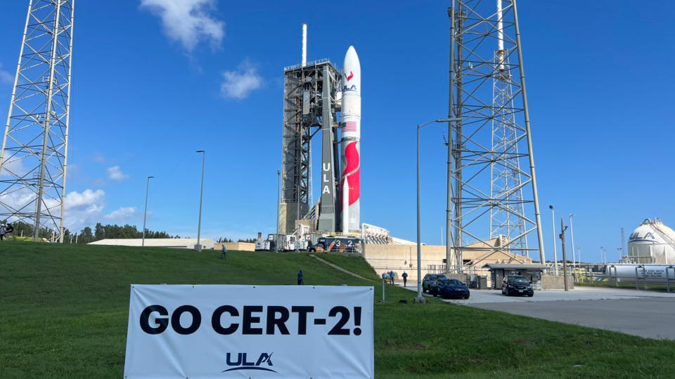  A white and red rocket stands on the launch pad under blue skies. 