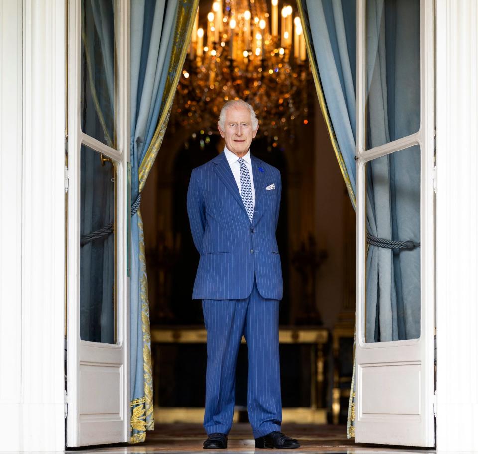 King Charles stands in front of an open door frame.