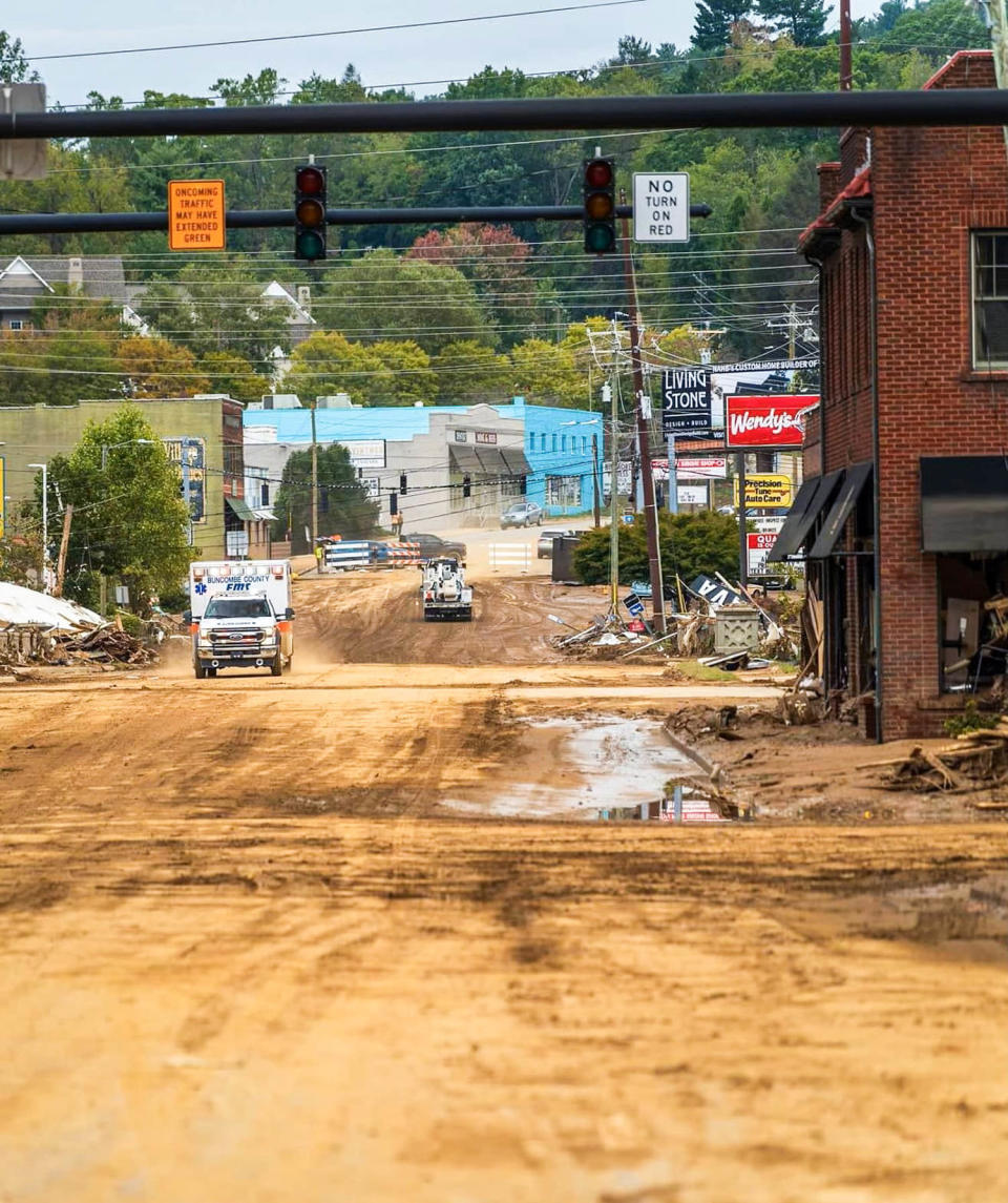 An ambulance drives on a dirt road between buildings (Stirling Barlow)